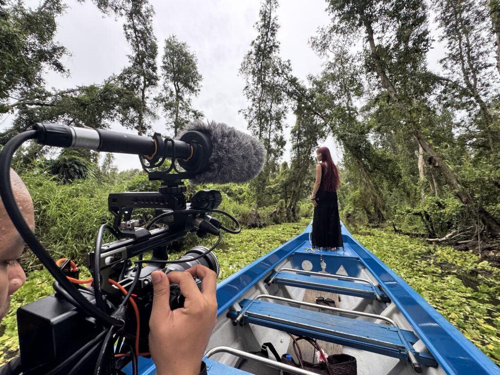 Film crew travelling by boat through a forested Mekong Delta waterway